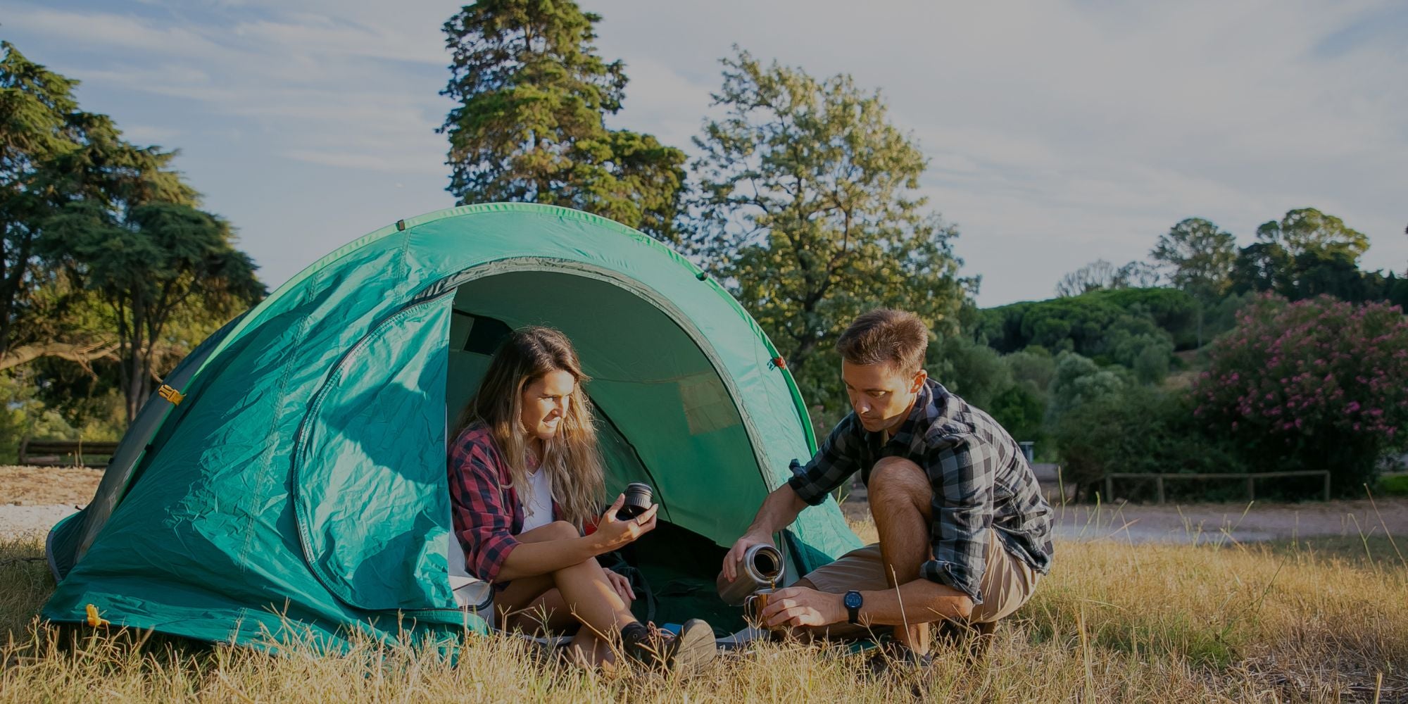Two people sitting inside a green tent in a natural setting with trees and grass.