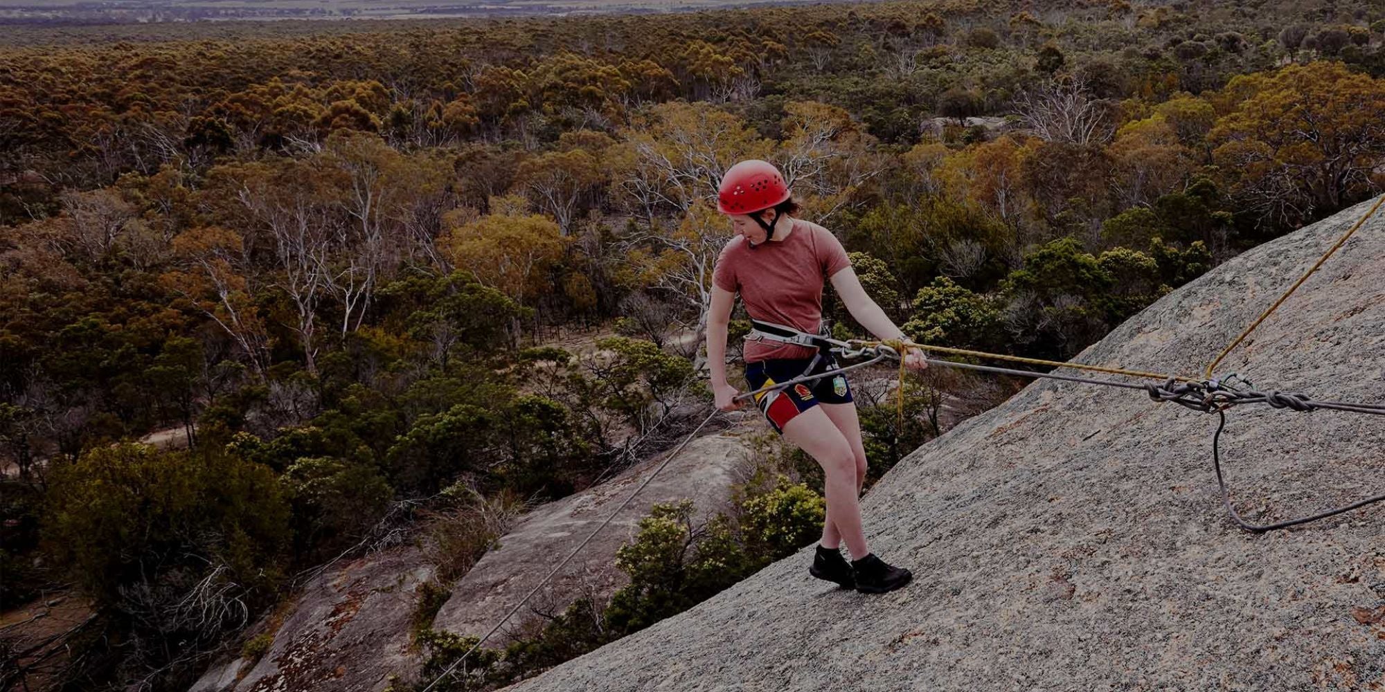 Person rock climbing on a rocky outcrop with a scenic landscape in the background